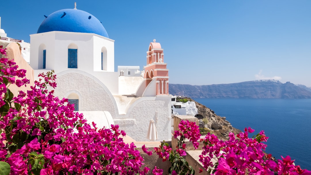 Blue-domed church and pink bougainvillea above the sea in Santorini, Greece